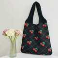Knitted black tote bag with red cherry pattern and green leaves in a clean interior setting - Black