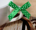 Detailed view of a green polka dot satin ribbon bow tied on a white cup handle - Green