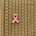 Detail of pink enamel ribbon brooch with gold metal edges on a textured woven background - Gold Base Pink