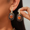 Detalle macro de pendientes de esmalte retro con piedra naranja y acentos dorados - Pendientes de aguja de plata / Marrón