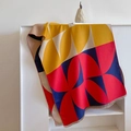Detail of color-block geometric knit shawl featuring decorative fringe edges on white stand - Red