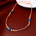 Detalle de collar chapado en oro de 18K con cuentas azules sobre tela marrón rojizo - Collar - Dorado - Azul - Chapado en oro real