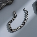 Pulsera de cadena bizantina de acero inoxidable plateado para hombre sobre rocas grises - Eslabón de Tejido Bizantino Plateado