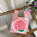 Close-up of pink knitted tote bag featuring a cute peach pattern on fluted glass surface - Peach Pink