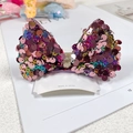 Detailed view of sequin bow hair clip with golden ribbon and origin card on magazine - Multi-color