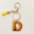 Detail of Letter D acrylic keychain with honey bee pattern, gold clasp and yellow tassel - Letter D