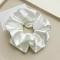 Detail of a creamy white glossy satin hair scrunchie with soft pleated texture on a tray - White