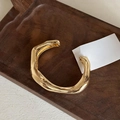 Detail of an irregular golden open arm cuff bracelet placed on a dark wooden tray - Irregular Lava Style - Gold