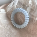 Detailed view of light blue translucent spiral telephone cord hair tie on textured paper - Screen Printed Blue