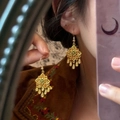 Close-up van gouden boho oorbellen met groene edelstenen en kleine hangertjes - Holle Groene Steen Oorhaak Stijl / Goud