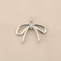 Macro shot of silver bow pendant on silk fabric showing smooth metal texture and detail - PJ0132-Silver Bowknot