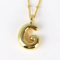 Close-up of golden letter G pendant necklace with polished finish on white background - Letter G
