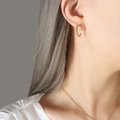 Orecchini a cerchio intrecciati dorati in acciaio al titanio indossati da una modella da vicino - Piccoli Orecchini d'Oro / Diametro 1,7 cm