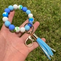 Blue and marble silicone bead bracelet with gold ring and tassel held outdoors - Blue Marble Pattern Combination (A2)