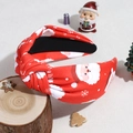Close-up of red knotted headband with Santa Claus and snowflake patterns on a wooden base - Red Santa Claus