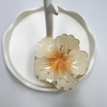 Elegant amber flower hair claw clip displayed on a white decorative jewelry stand tray - Light Orange (Rolled Flower)