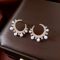 Detailed view of gold plated C-shaped pearl earrings with cubic zirconia on jewelry box - Gold