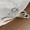Detailed view of a silver alloy bow hair claw clip placed on textured white paper - Silver