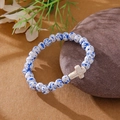 Blue spotted beaded bracelet with white cross charm on a rustic background - White Blue Spotted White Cross Bracelet