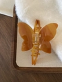Elegante vlindervormige haarklem van acetaat in amberbruin op zachte stoffen ondergrond - Karamel Textuur
