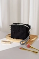 Close-up of a black distressed cotton linen cosmetic bag with woven handle on a wood tray - Black Pillow Bag