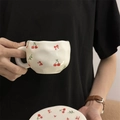 Hand-painted ceramic coffee cup with red cherry and bow patterns, held by hand - Colorful Cherry Blossom