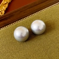 Macro shot of polished round pearl earrings on green fabric with vintage wooden frame - Greyish White Lustrous Pearl Studs