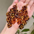 Handheld view of acrylic leopard print tassel earrings with amber resin layered petals - Leopard Petal Tassel Style / Brown