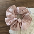 Pink satin scrunchie with ruffled edges on white lace and dark wood surface - Pink