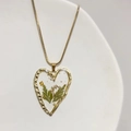 Detailed close-up of heart-shaped gold pendant with resin and green botanical leaf inserts - Heart With Dried Flowers