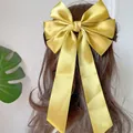 Eleganter großer gelber Satin-Schleifen-Haarclip mit langen Bändern auf lockigem Haar - Ingwergelb