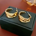 Macro detail of golden irregular wave-pattern earrings on a premium black leather box - Gold
