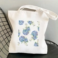 White canvas tote bag featuring blue hydrangea watercolor print on a black mesh chair - Blue Hydrangea