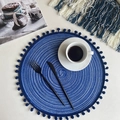 Blue round hand-woven cotton coaster with small pompoms on white desktop setting - 38cm Placemat / Blue