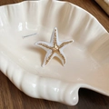 Macro view of a white starfish ring with golden accents on a ceramic shell tray - White