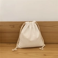 Close-up of minimalist cream cotton linen drawstring bag on a natural wooden table - Small / Beige