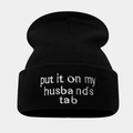 Detailed close-up of ribbed knit beanie with white 'put it on my husband's tab' embroidery - Black