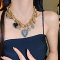 Collana a catena dorata spessa con ciondoli a cuore e farfalla vintage su una modella - Collana Vintage in Oro con Ciondoli a Cuore e Farfalla