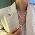 Detail of elegant pearl necklace with bow accent worn on a female model with blazer - Gold Small Pearl Necklace