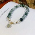Primer plano de pulsera de cristal fantasma verde y perlas sobre fondo de libro - Caja de Regalo Exquisita / Cristal Fantasma Verde y Perla de Agua Dulce