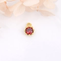 Detail of 18k gold plated crown pendant with a red zircon stone on white surface - Red