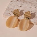 Close-up of golden metal studs with beige acrylic pendant on a beige stone surface - Brown