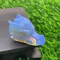 Blue semi-transparent dragon head crystal carving placed on natural wood surface - Blue Opalite