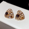 Vista macro de pendientes triangulares dorados con gemas marrones y cristales brillantes - Marrón dorado