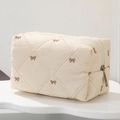 Close-up of quilted cosmetic bag with brown bow embroidery and metal zipper detail - Beige