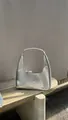 Détail du sac hobo croissant argenté métallisé avec finition miroir sur une surface - Argenté