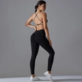 Detail van sportbeha met kruisbandjes en yoga leggings in naadloos zwart functioneel stof - S / Zwart