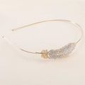 Serre-tête plume doré élégant orné de strass brillants sur fond beige doux - Plume Or