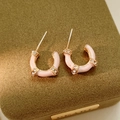Makro-Detail von U-förmigen rosa Emaille-Ohrringen mit Vergoldung und funkelnden Kristallen - Silber-Ohrstecker - Rosa