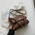 Dark brown quilted crossbody bag with gold chain strap and turn-lock on a blazer - Brown